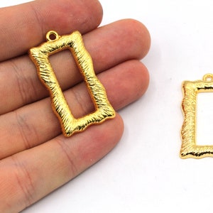 May include: Two gold-colored metal rectangular picture frame charms with a textured surface. The charms have a loop at the top for hanging.