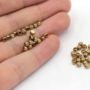 Könnte beinhalten: Ein Haufen kleiner, goldfarbener Metallperlen. Die Perlen sind quadratisch mit einem Loch in der Mitte.