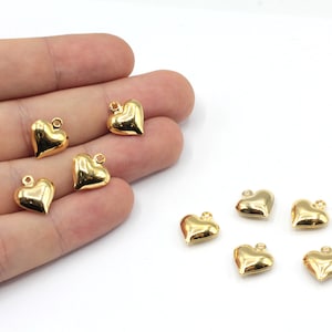 May include: Eight gold-colored heart-shaped charms with a loop at the top. The charms are arranged in two rows on a white surface.