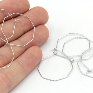 May include: Two pairs of silver octagon hoop earrings. The earrings are made of thin wire and have a simple, modern design.