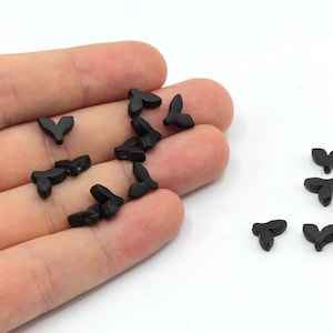 Könnte beinhalten: Eine Sammlung schwarzer, blattförmiger Perlen. Die Perlen sind klein und haben eine glatte, matte Oberfläche.