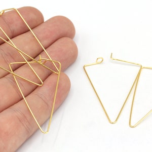 May include: Gold-colored geometric earrings. The earrings are in a triangular shape, with a thin wire frame. The earrings are shown against a white background. The earrings are a simple, modern design.