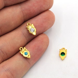 Op de afbeelding: Drie goudkleurige bedels met verschillende gekleurde edelstenen. De bedels zijn traanvormig met een decoratief ontwerp. De edelstenen zijn helder, turquoise en groen.