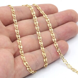 Könnte beinhalten: Eine goldene Kettenkette mit Diamantenschliff. Die Kette wird auf einer Hand gezeigt, wobei drei Stränge der Kette sichtbar sind.