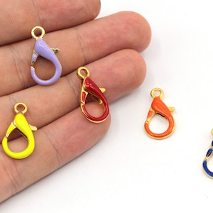 May include: Five gold-toned metal lobster clasps with enamel accents. The clasps are in different colours: purple, red, orange, yellow, and blue.