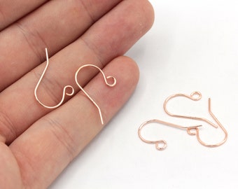 May include: Four rose gold earring hooks, two are held in a hand and two are laying on a white surface.