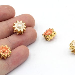 May include: Three gold-toned flower charms with a white pearl center. Two charms are orange and one is white.
