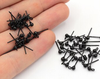 May include: A pile of black earring findings with a small ball at the end of each pin. The findings are arranged in two piles on a white surface.