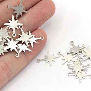 Puede incluir: Un montón de dijes en forma de estrella plateados con un anillo de salto para sujetar a joyas u otras artesanías.