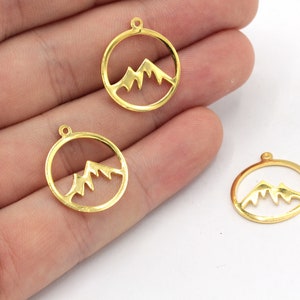 May include: Three gold-colored metal charms in the shape of a circle with a mountain range silhouette inside.