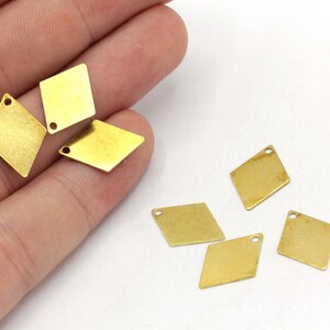 May include: A group of six gold-coloured diamond-shaped metal charms with a hole at the top for attaching to jewellery or other crafts.