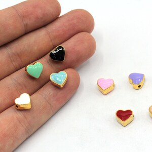 May include: Assortment of colorful enamel heart charms with gold accents. The charms are in various colors, including black, white, pink, red, blue, green, and purple.