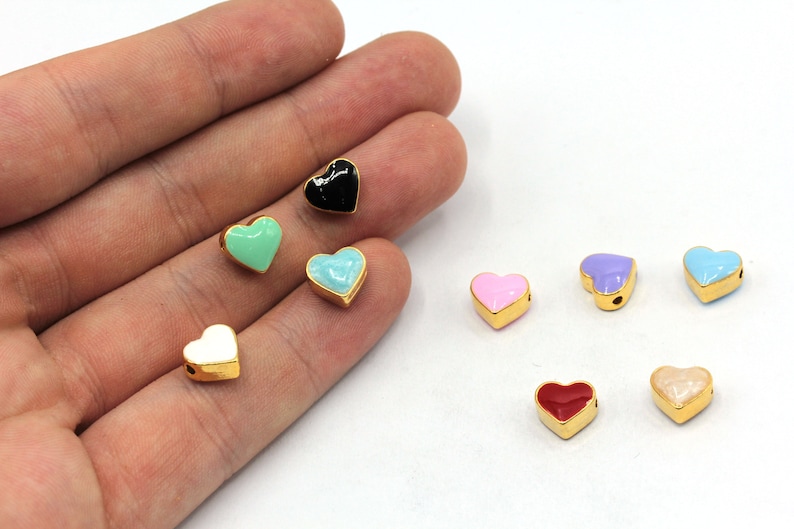 May include: Assortment of colorful enamel heart charms with gold accents. The charms are in various colors, including black, white, pink, red, blue, green, and purple.