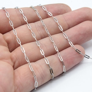 May include: Silver chain with a link style that resembles paper clips. The chain is shown on a hand, with multiple strands of the chain.