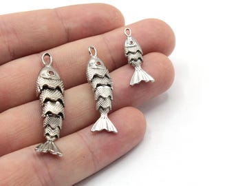 May include: Three silver fish charms with red accents. The charms are different sizes and are hanging from a hand.