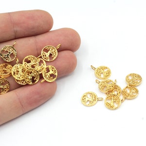 Op de afbeelding: Een groep gouden metalen bedels met een levensboomontwerp. De bedels hebben een lus aan de bovenkant om aan sieraden of andere knutselprojecten te bevestigen.