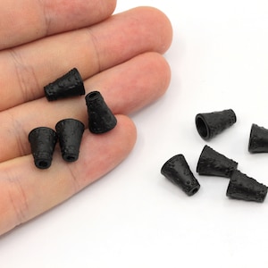 May include: Ten black plastic cord end caps with a textured surface. The caps are cone-shaped and have a small hole at the top.