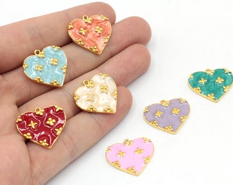 Puede incluir: Seis dijes de corazón de oro con diferentes esmaltes de colores y patrones florales dorados. Los dijes están en una mano.