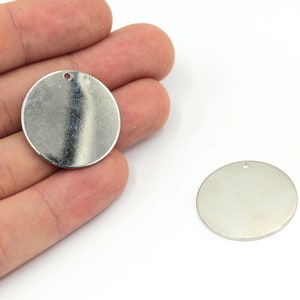 May include: Two silver metal round blank tags with a hole at the top. The tags are smooth and shiny.