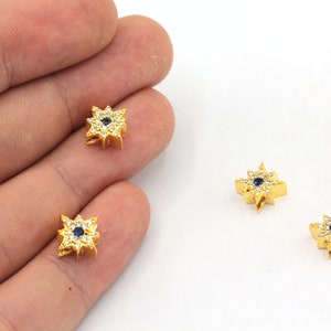 May include: Three gold-toned starburst charms with a blue center stone and clear stones around the edge.