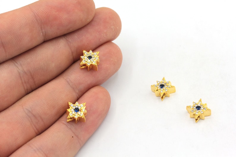 May include: Three gold-toned starburst charms with a blue center stone and clear stones around the edge.