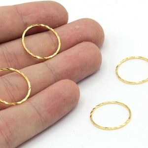 May include: Close-up of several gold-coloured, textured, open circle jewellery components. The rings have a twisted design and are displayed against a white background. These components are likely used for jewellery making.