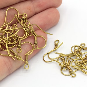 May include: A collection of gold-colored earring hooks, featuring a curved hook design with a small coil and bead detail. The hooks are shown against a white background, suggesting a craft or jewelry-making theme.