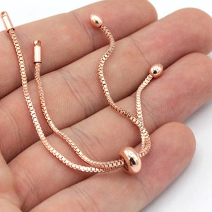 May include: A rose gold chain bracelet with a sliding bead closure. The bracelet is made of a delicate chain and has a simple, elegant design.