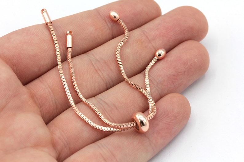 May include: A rose gold chain bracelet with a sliding bead closure. The bracelet is made of a delicate chain and has a simple, elegant design.