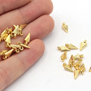 May include: A collection of gold-toned triangle-shaped metal charms with a textured surface. The charms have a loop at the top for attaching to jewelry or other crafts.