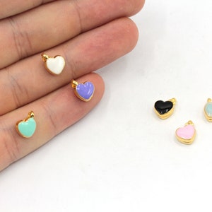 Puede incluir: Surtido de dijes de corazón de esmalte en varios colores, incluyendo blanco, morado, negro, azul claro y rosa. Cada dije tiene un marco de metal dorado y un bucle para sujetarlo a joyas.