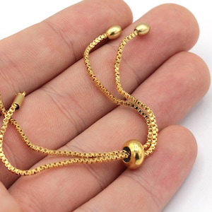 May include: A gold chain bracelet with a sliding bead closure. The bracelet is made of a delicate chain and has a simple, elegant design.
