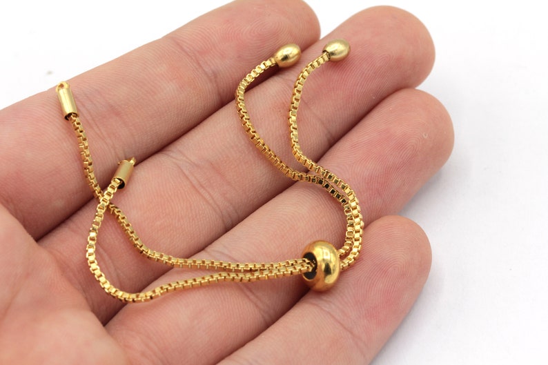May include: A gold chain bracelet with a sliding bead closure. The bracelet is made of a delicate chain and has a simple, elegant design.