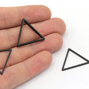 May include: Three black metal triangle shapes, each with a hollow center, are displayed on a hand. The triangles are approximately 1 inch in size.