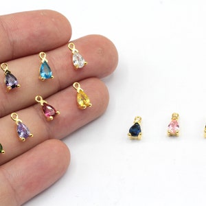 May include: A selection of teardrop-shaped charms with gold settings and gemstones in various colours. Gemstones include red, purple, blue, white, yellow, pink, green, and teal. The small charms are suitable for jewellery making.