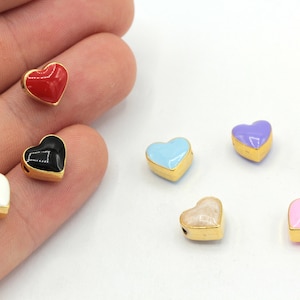 May include: Assortment of colorful enamel heart charms with gold accents. The charms are in various colors, including red, black, white, light blue, lavender, green, and pink.