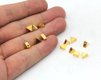 May include: A collection of gold-toned metal triangle-shaped beads with a hole in the center. The beads are scattered on a white surface.
