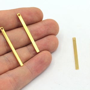 May include: Five gold metal bar pendants with a small hole at the top. The pendants are approximately 1 inch long.