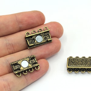 May include: Three antique bronze magnetic clasps. Each clasp is rectangular with a decorative pattern and small loops on each end. A silver-colored magnet is visible on the front of each clasp. The clasps are designed for jewelry making.