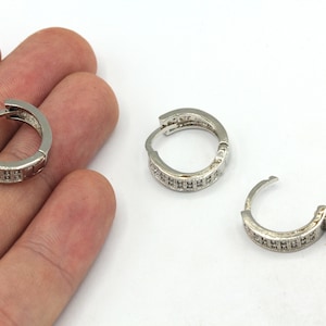May include: A pair of silver hoop earrings with a row of small clear stones around the edge.