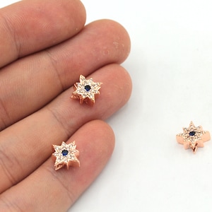 May include: Three gold-tone star-shaped charms with clear and blue crystals. The charms have a small blue eye in the center.