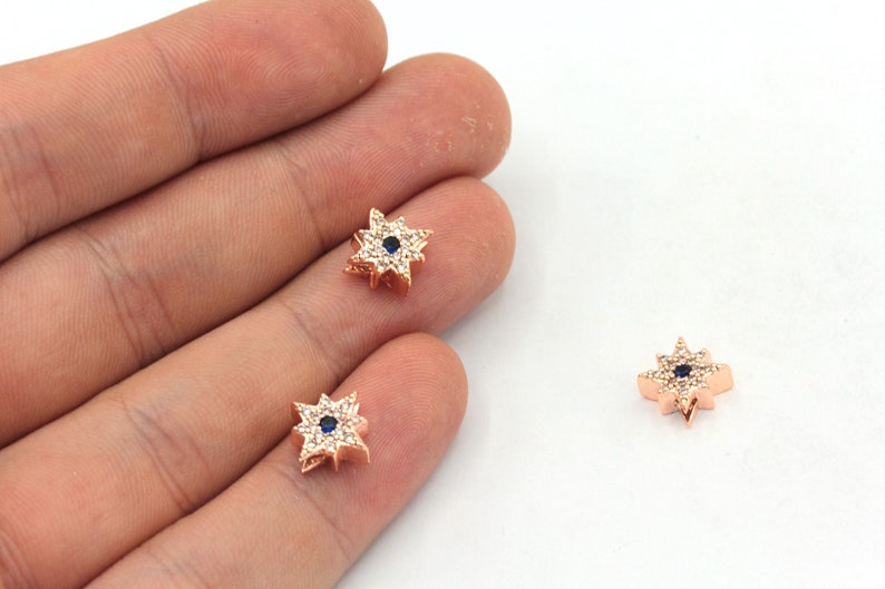 May include: Three gold-tone star-shaped charms with clear and blue crystals. The charms have a small blue eye in the center.