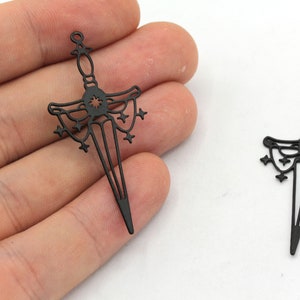 May include: Two black metal sword charms featuring a star design. The swords are detailed with a starburst at the hilt and a decorative design on the blade.