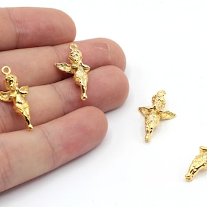 May include: Four gold-coloured angel charms with wings and a loop for hanging. The charms are on a hand, with the fingers spread out.