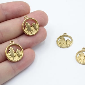 May include: Gold-colored metal pendants featuring a circular frame with a cut-out design of three stylized pine trees. The pendants have a small loop at the top for attaching to a chain or other jewelry component. The image shows several of these pendants.