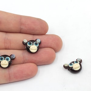 May include: Three brown glass monkey head beads with white faces and blue eyes. The beads are about 1 inch in diameter.