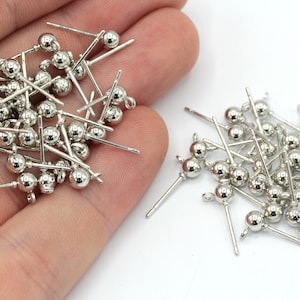 May include: A pile of silver-toned earring posts with small round balls on the end. The posts are about 1 inch long.
