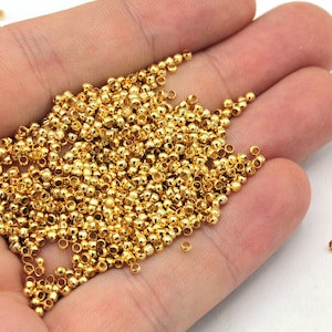 May include: A large pile of small, round, gold-colored beads in a hand. The beads are smooth and shiny.