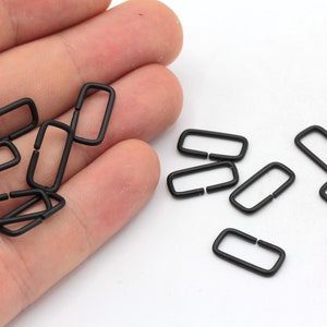 May include: A close-up of a pile of black metal D-rings. The rings are small and have a smooth finish.