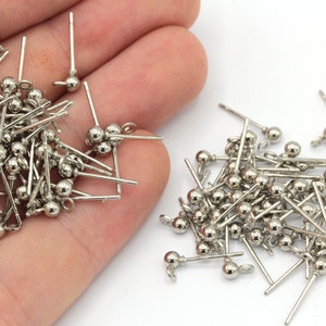 May include: A pile of silver-toned earring posts with small round balls on the ends. The posts are about 1 inch long.